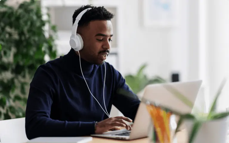 Man wearing white headphones at his desk while joining a call on his laptop