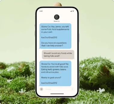 Smartphone displaying a text conversation about folic acid supplements from Stone Co. on a grassy surface.