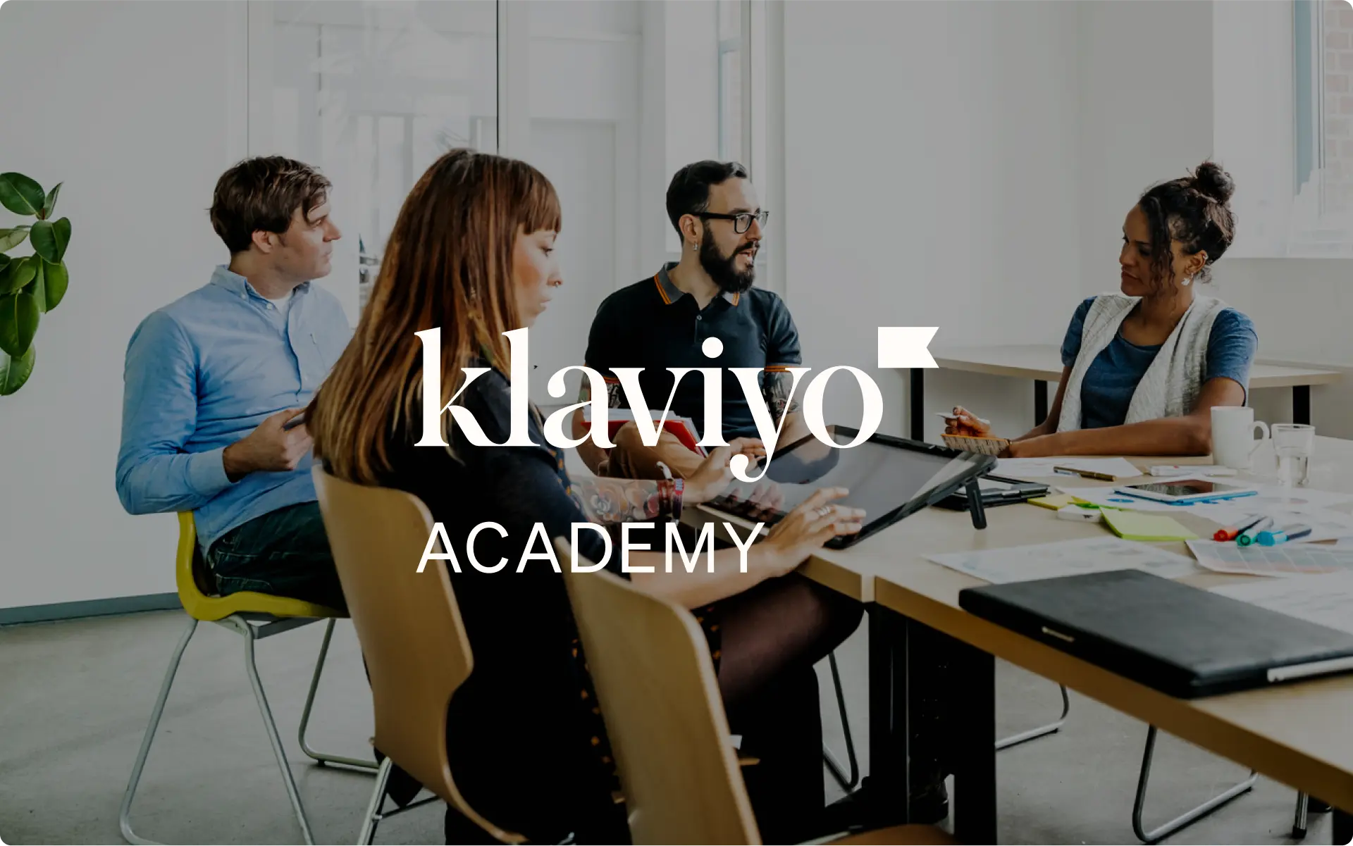 Group of professionals in a modern office collaborating, with 'Klaviyo Academy' text overlay, representing educational resources for Klaviyo users.