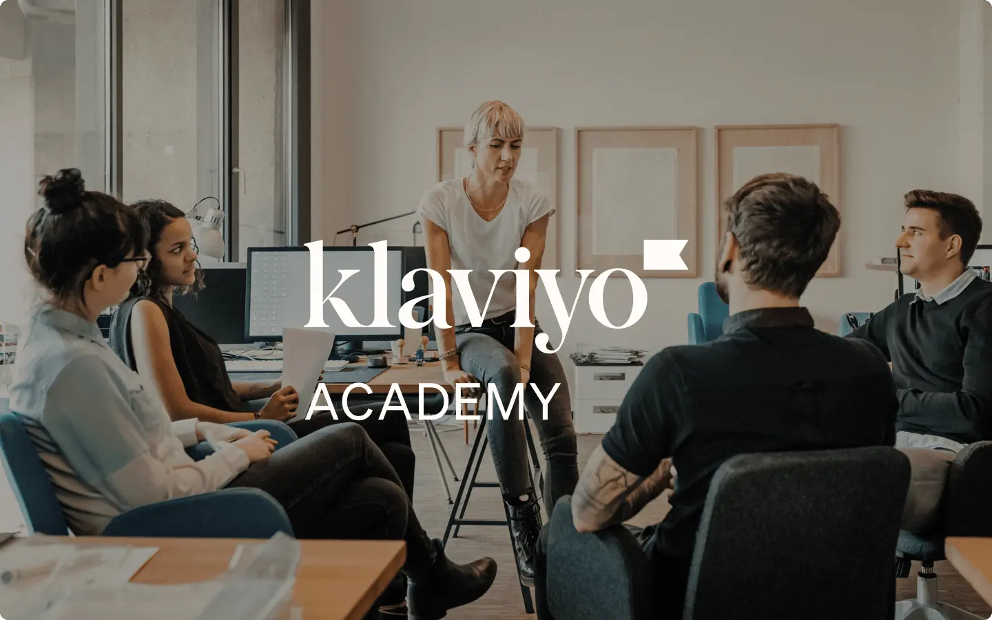 Klaviyo Academy logo over five coworkers have a meeting in an open office plan