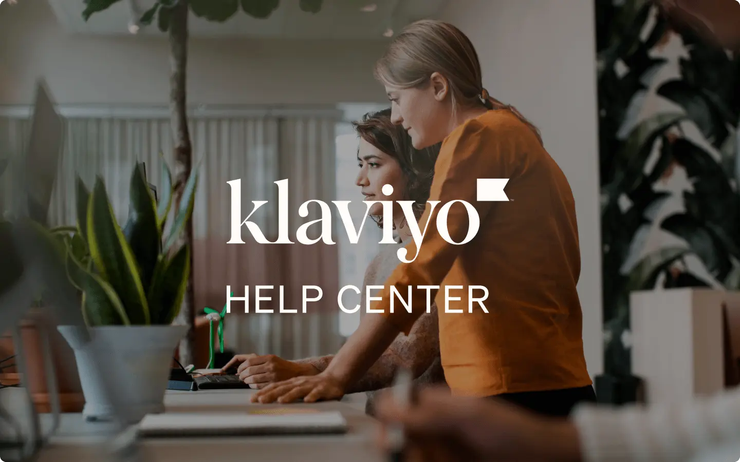 Two coworkers collaborating at a standing desk in a bright, airy office with Klaviyo Help Center text overlay